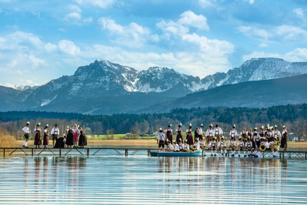 Trachtler am Steg des Waginger Sees Gruppenbild im Frühling und im Hintergrund schneebedeckte Berge